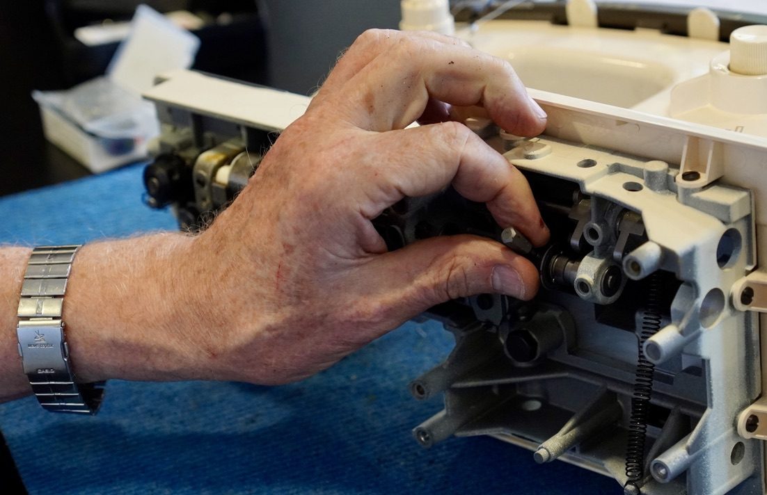 Hand bei der Reparatur einer geöffneten Nähmaschine auf der Werkbank
